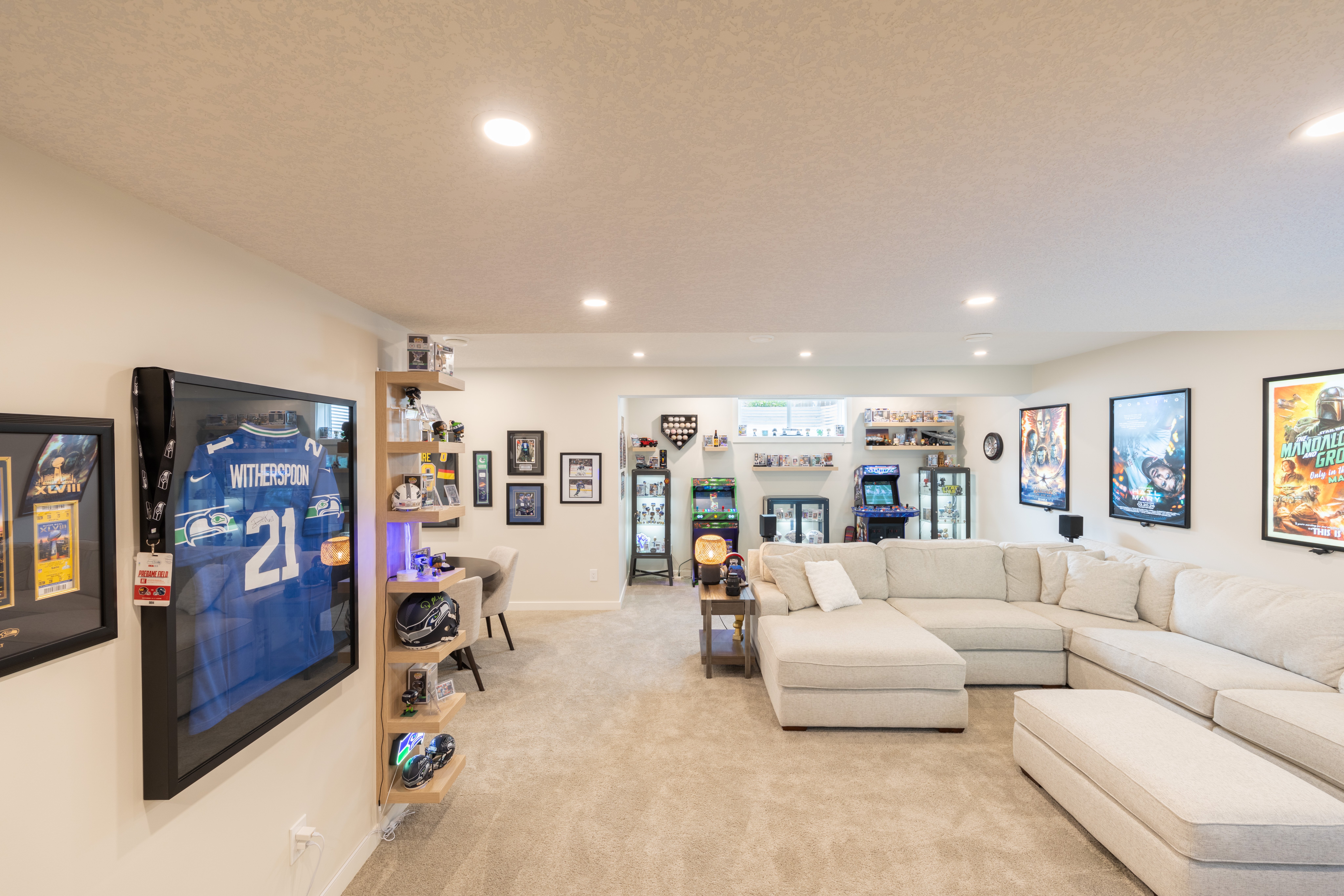 The open recreation area connects sectional seating, arcade games, memorabilia displays, and the adjacent games table.