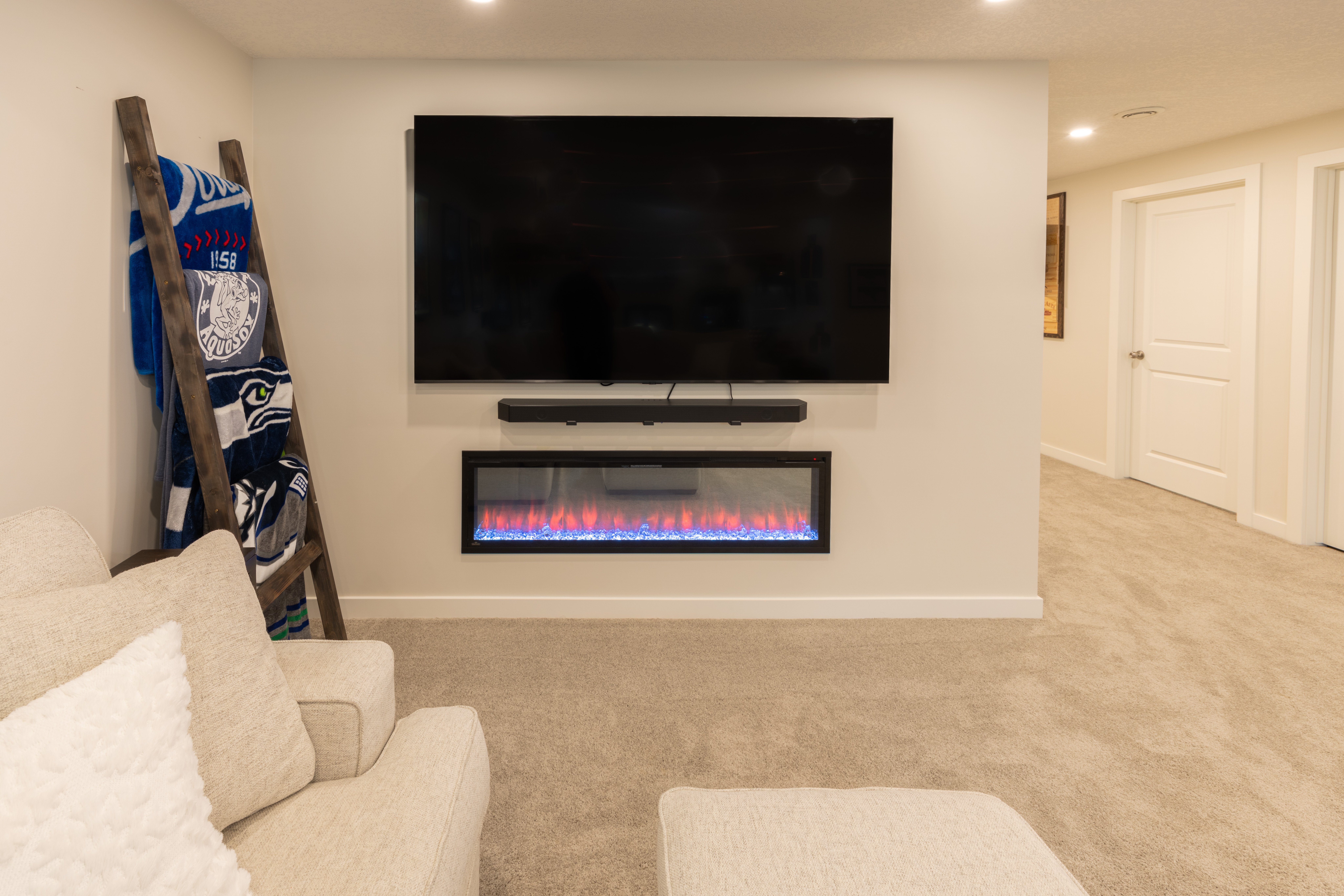 A wall-mounted television and soundbar sit above the recessed Napoleon electric fireplace on a simple neutral media wall.