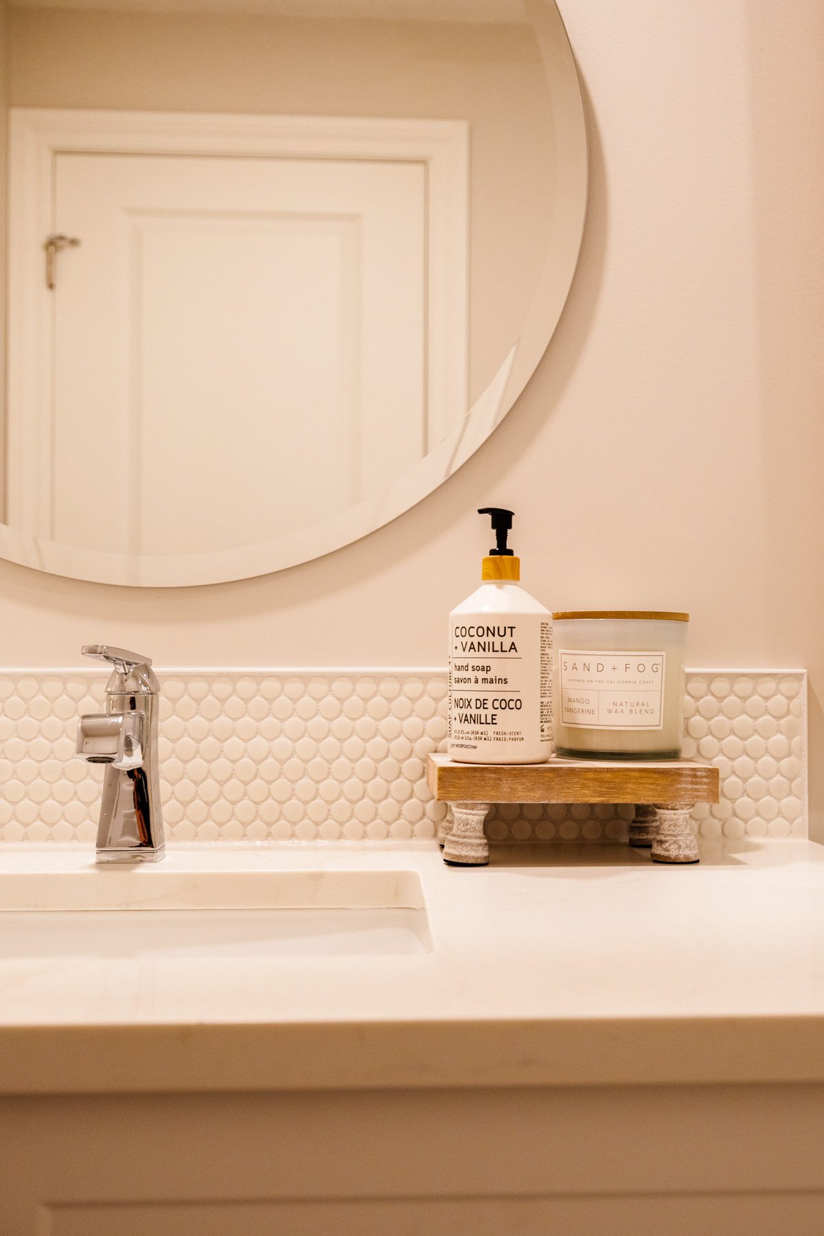 Detailed view of the white vanity, black faucet, round mirror, and textured light tile backsplash.