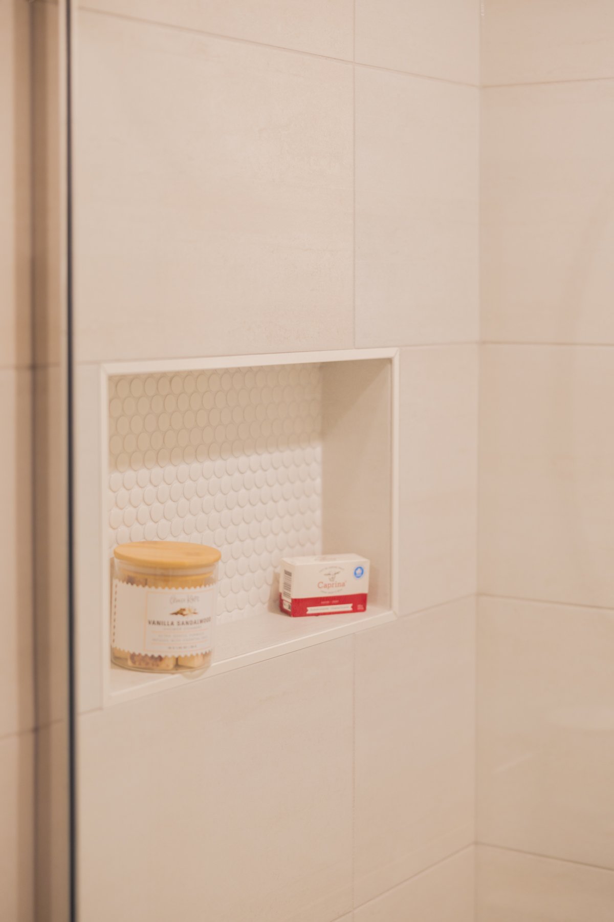 A built-in shower niche finished with light mosaic tile adds both storage and visual texture.