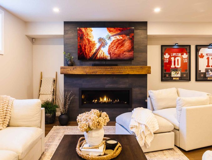 The media room includes a linear fireplace, mounted TV, bubble hockey table, and framed hockey jerseys.