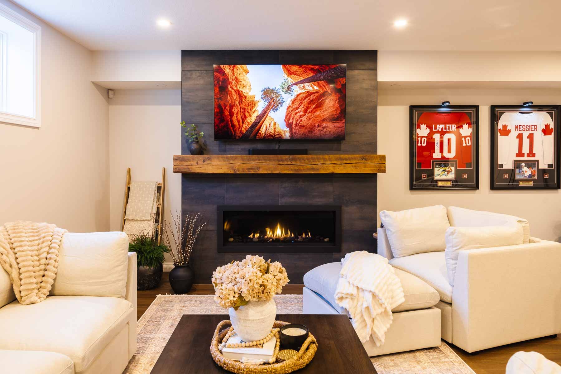 The media room includes a linear fireplace, mounted TV, bubble hockey table, and framed hockey jerseys.