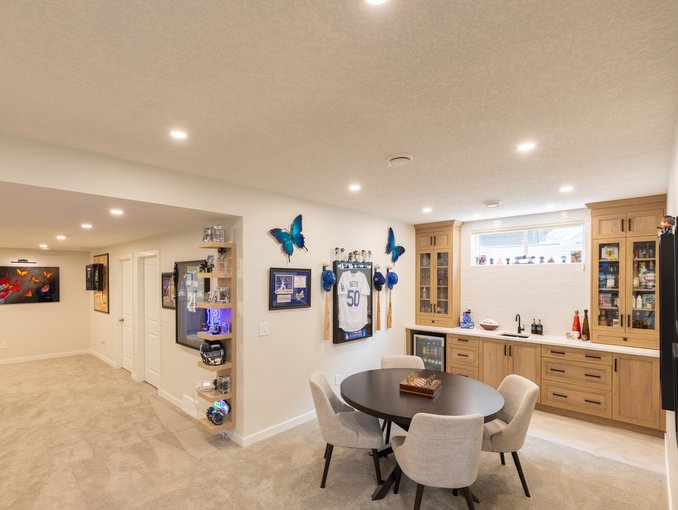A wide view shows the games table, wet bar, sports displays, and open passage connecting the entertaining spaces.