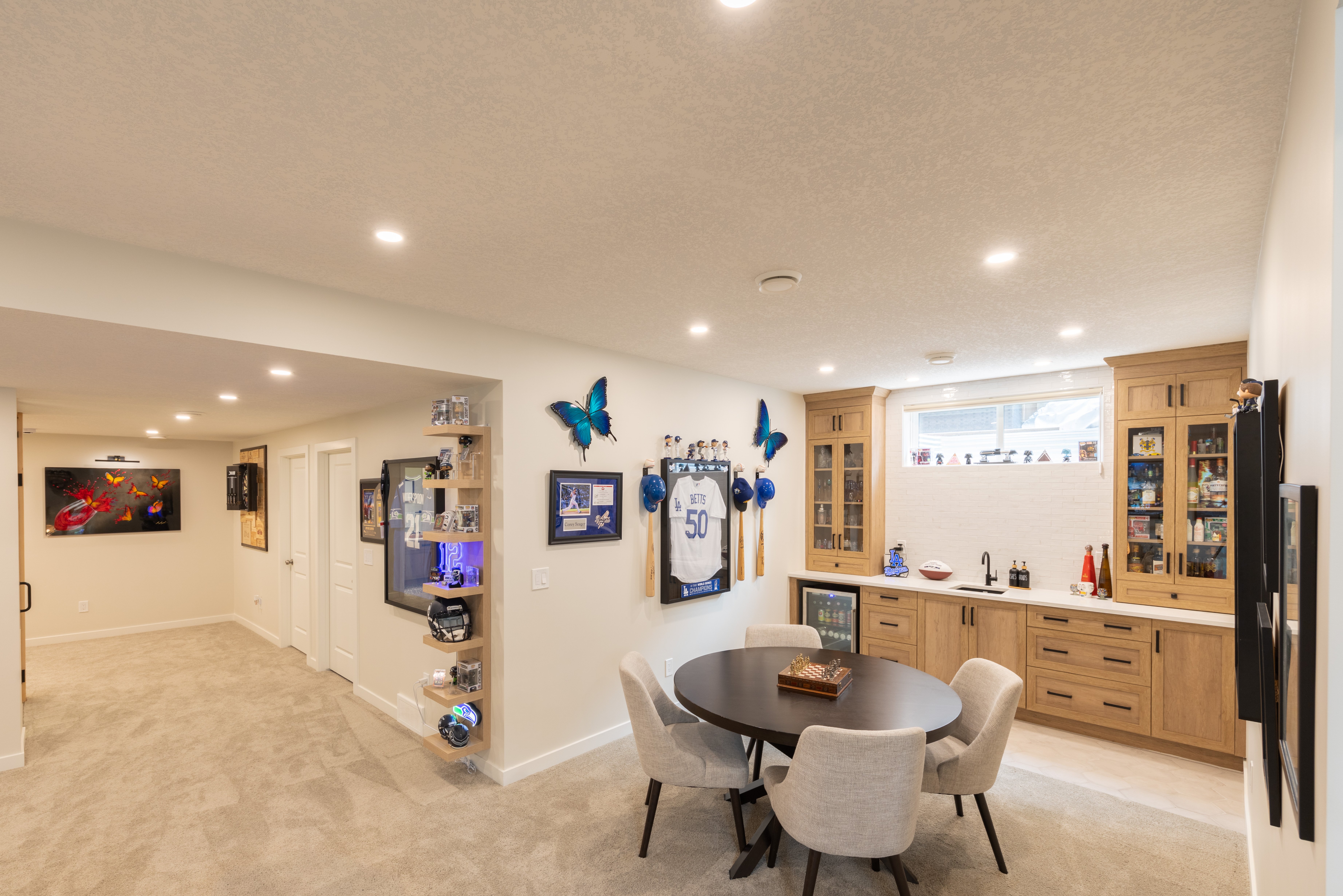 A wide view shows the games table, wet bar, sports displays, and open passage connecting the entertaining spaces.