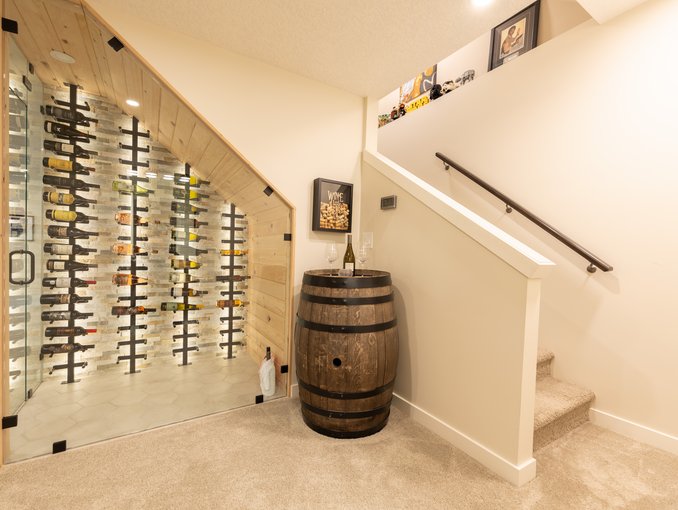 Carpeted steps and a dark handrail rise beside the glass wine enclosure and decorative barrel accent.