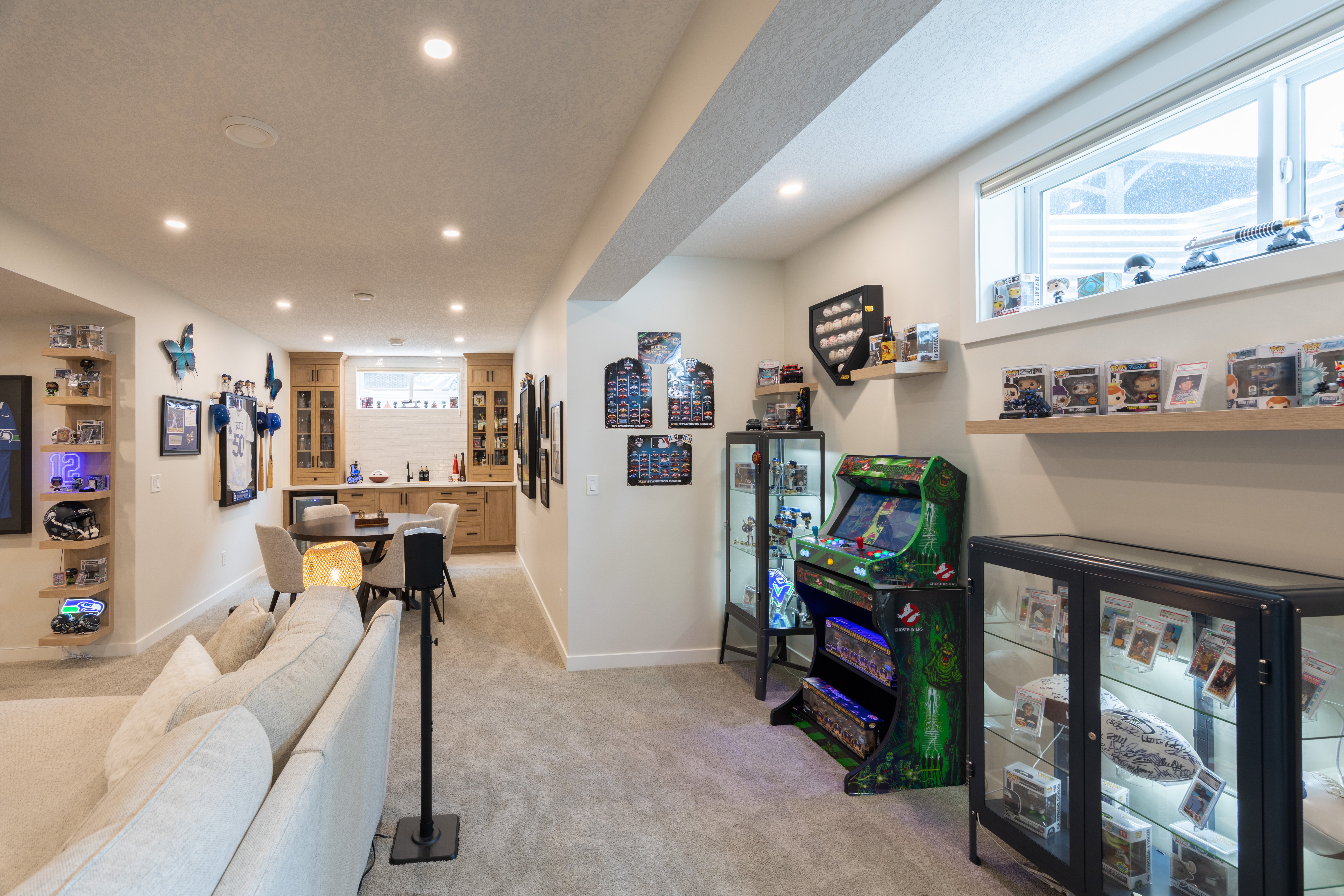 A view along the sectional toward the arcade displays, games table, and wet bar shows the connected recreation layout.