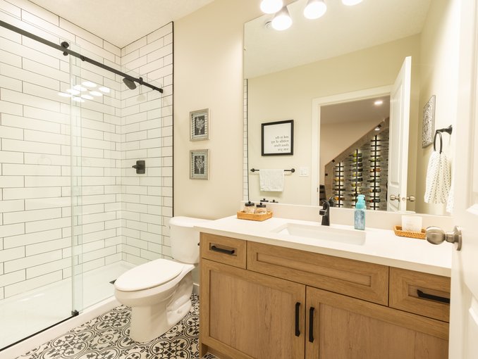 A white countertop and black faucet top the wood-tone vanity beside a clear glass shower with white subway tile.
