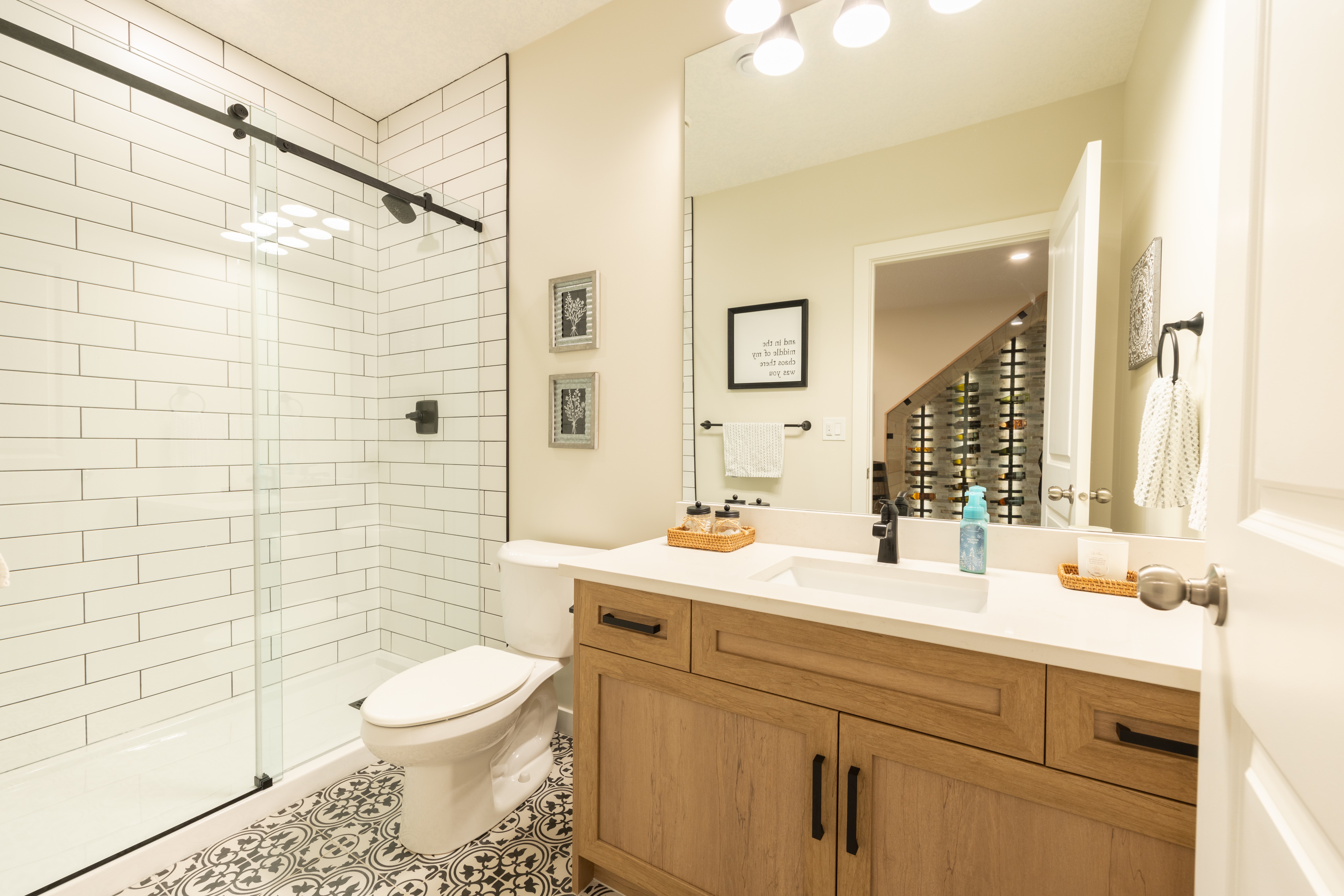 A white countertop and black faucet top the wood-tone vanity beside a clear glass shower with white subway tile.