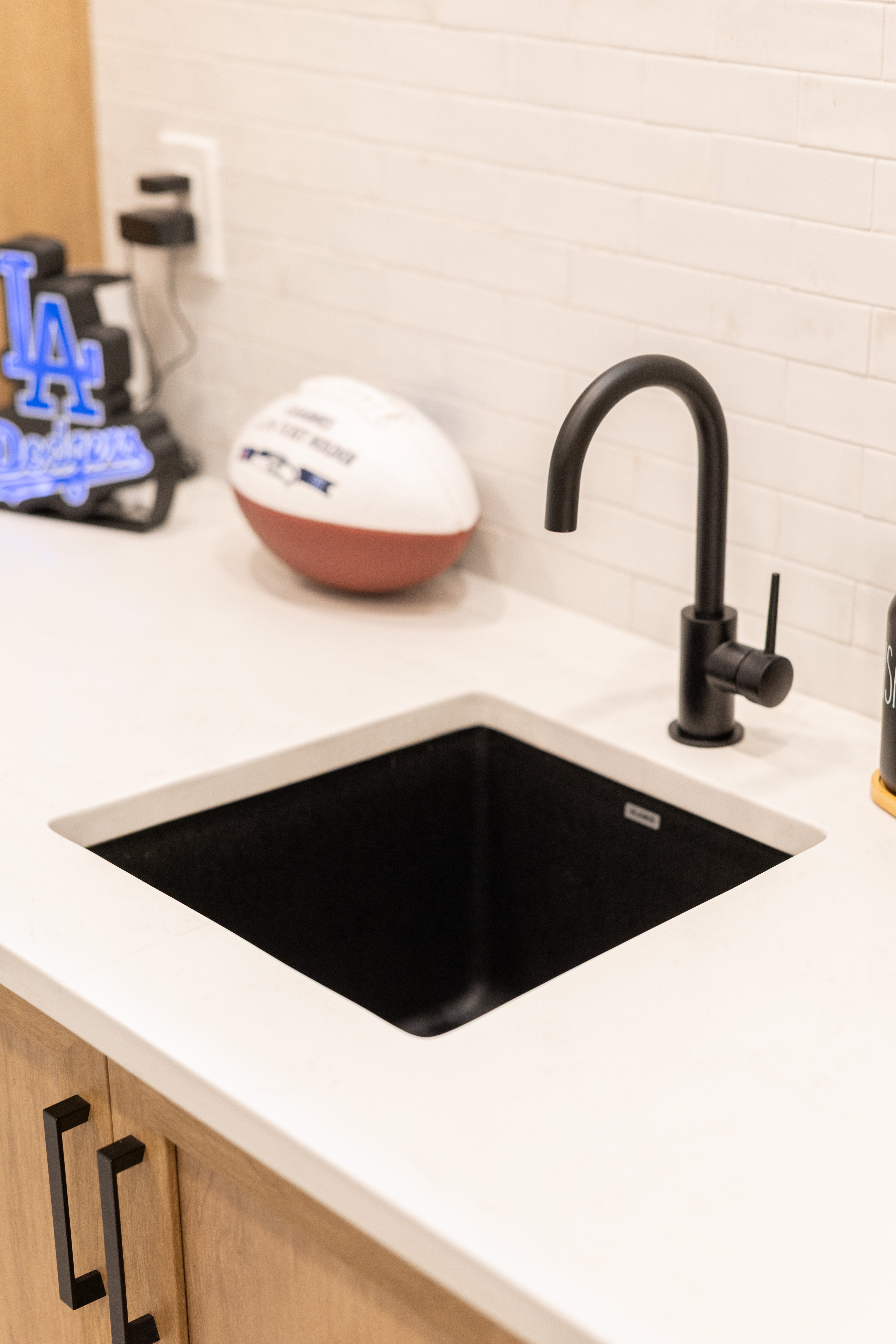 A black undermount sink and curved faucet contrast with the white countertop and subway-style backsplash at the wet bar.