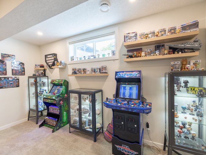 Arcade games, illuminated glass cabinets, and floating shelves create a dedicated display and gaming area beneath a basement window.